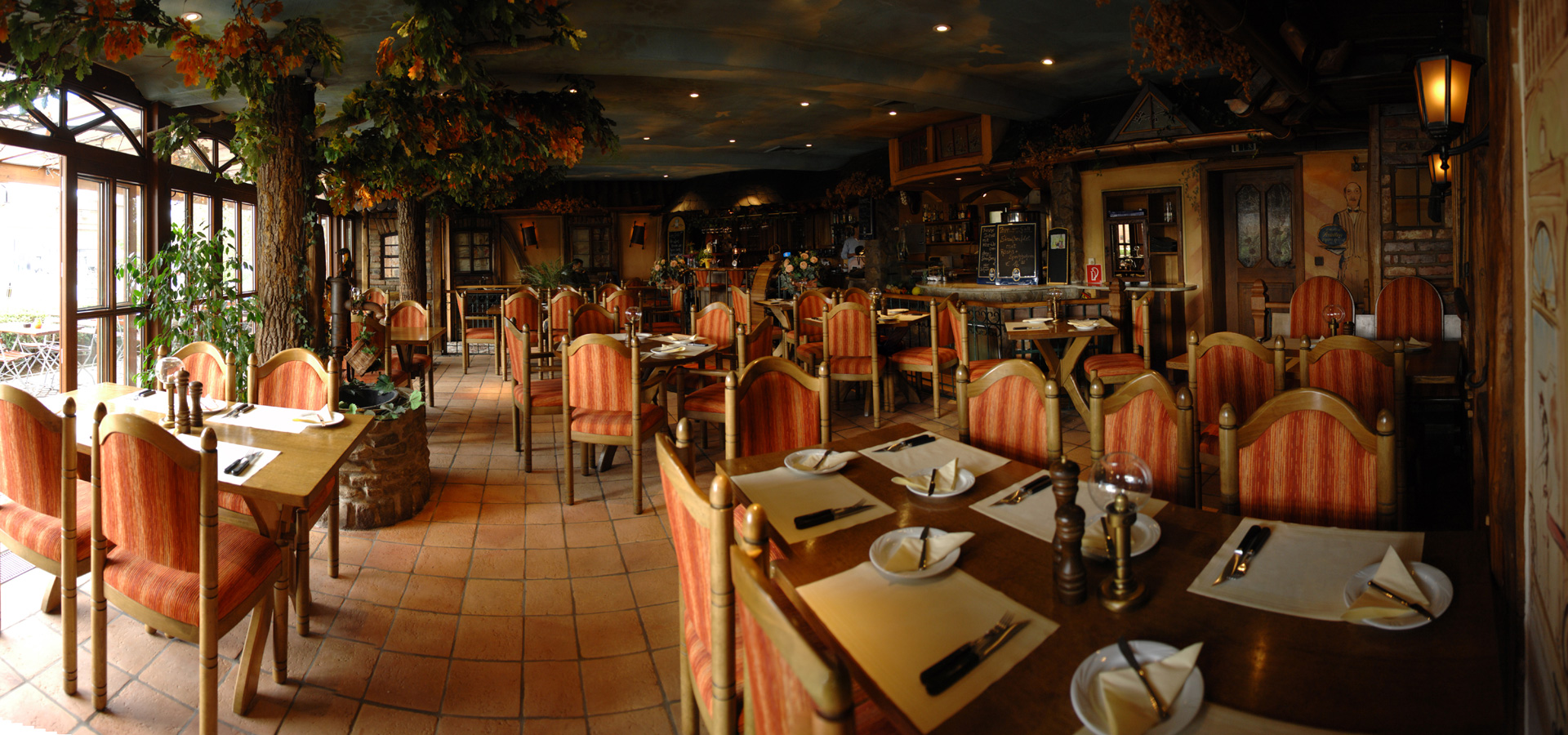 Gastraum des Steakhaus ANGUS mit Holzmöbeln, Terrakotta-Fliesen und Baumdekoration